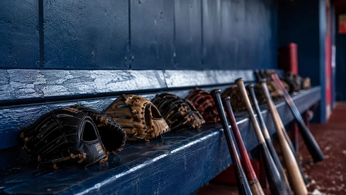 Baseball gloves and bats lined up on an empty dugout bench